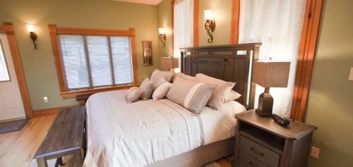 Cozy bedroom with a large bed, decorative pillows, wooden furniture, and soft lighting from wall sconces.