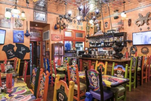 Colorful restaurant interior featuring vibrant chairs, decorative walls, and a bar with various bottles and artwork.