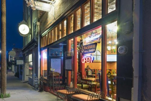 Exterior of Vaqueras Grill Cantina at night, featuring large windows, an "Open" sign, and colorful decor inside.