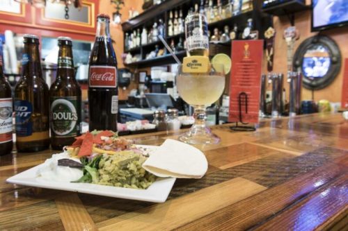 A bar counter with a plate of rice and toppings, drinks including beer and soda, and a cocktail in a glass.