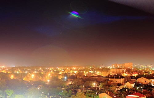 A nighttime cityscape with glowing lights from buildings and trees, creating a warm, vibrant atmosphere.