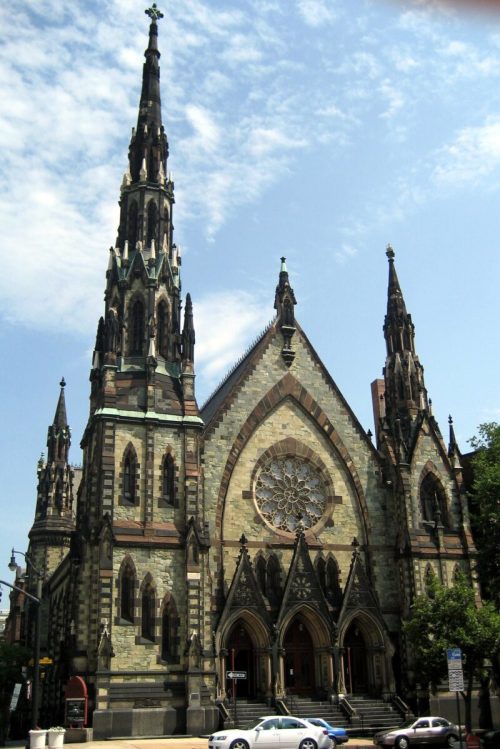 Gothic-style church with tall spires and intricate stonework, featuring a large rose window and a clear blue sky.