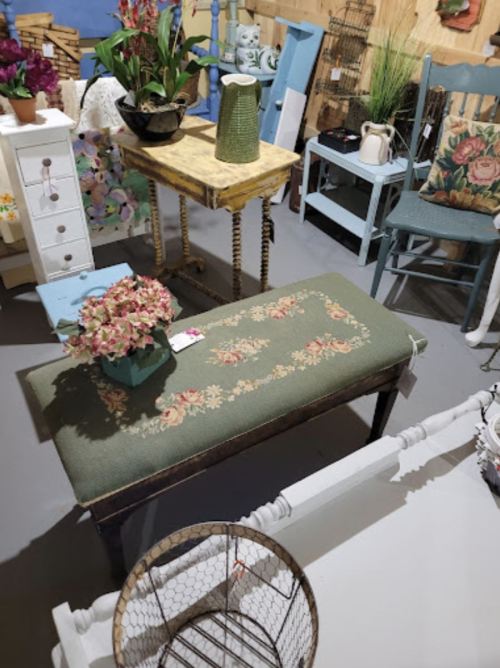 A cozy vintage display featuring a green upholstered bench, floral decor, and various furniture pieces in a charming setting.