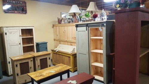 A cozy room filled with various wooden furniture pieces, including cabinets, shelves, and tables, all for sale.