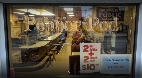 View of the Pepper Pod diner interior, featuring a counter, seating, and promotional signs for food deals.