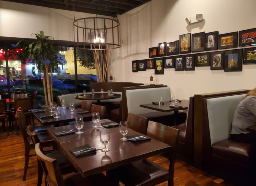 A cozy restaurant interior with wooden tables, chairs, and framed artwork on the walls, illuminated by soft lighting.