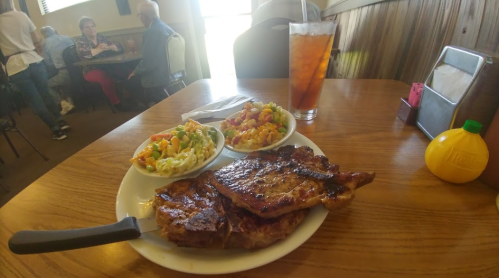 A plate with grilled meat, two bowls of salad, and a glass of iced tea in a cozy restaurant setting.