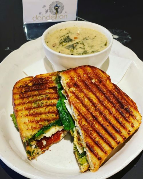 A grilled sandwich with spinach and tomato, served with a bowl of creamy soup on a white plate.