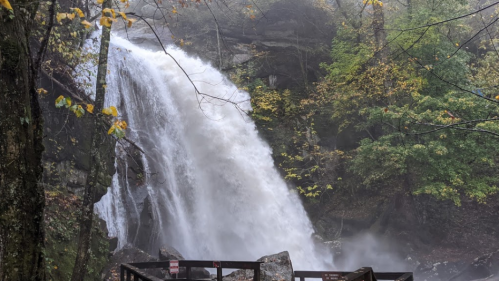A waterfall cascading down rocky cliffs, surrounded by lush green trees and mist in a serene natural setting.