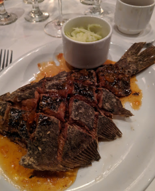 A whole grilled fish served on a plate with a side of coleslaw and a sauce drizzled over it.