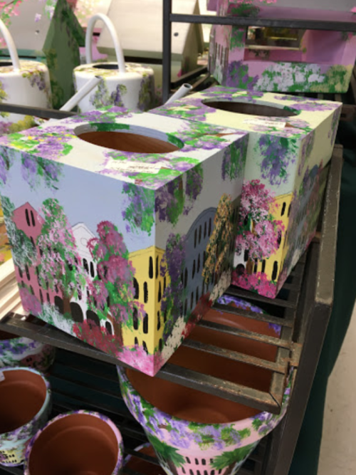 Colorful painted flower pots with floral designs displayed on a shelf, featuring various shapes and sizes.