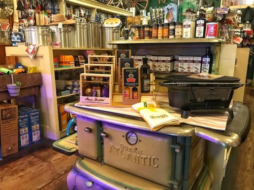 A vintage kitchen display featuring an old stove, shelves of products, and various kitchenware in a cozy shop setting.