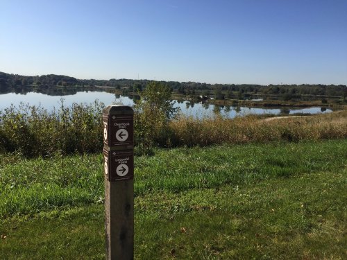 A scenic view of a lake surrounded by greenery, with a signpost indicating directions to an overlook and a loop trail.
