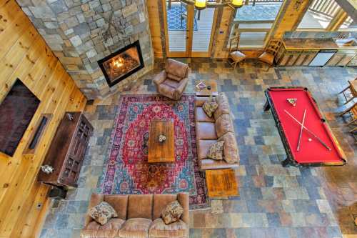 Cozy cabin living room with a stone fireplace, leather sofas, a pool table, and a colorful area rug.