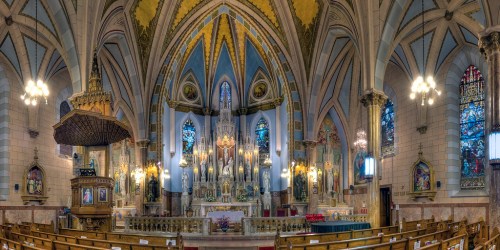 A panoramic view of a grand church interior featuring ornate arches, stained glass windows, and a beautifully decorated altar.