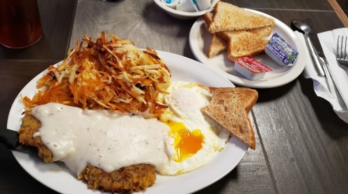 A plate of chicken fried steak with gravy, hash browns, eggs, and toast, served with butter and jam on the side.