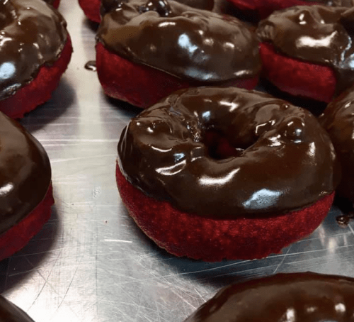 A close-up of red velvet donuts topped with shiny chocolate glaze, arranged on a silver tray.