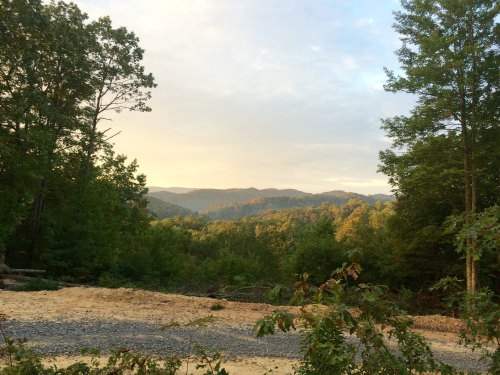 A scenic view of rolling hills and trees under a soft, cloudy sky during sunset.
