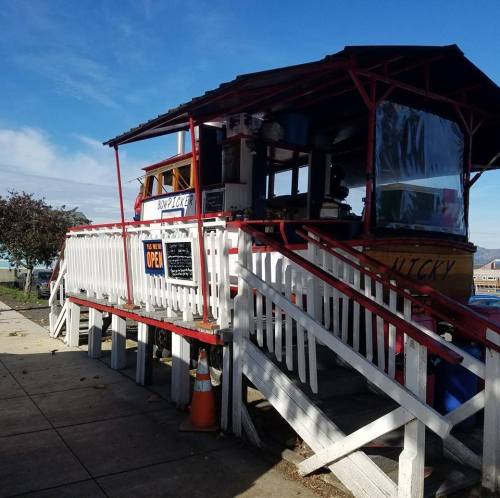 A small, elevated food stand with a red roof and white railing, featuring an "Open" sign and a view of the surroundings.