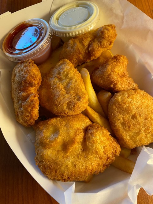 A takeout box filled with golden fried chicken nuggets and French fries, accompanied by dipping sauces.