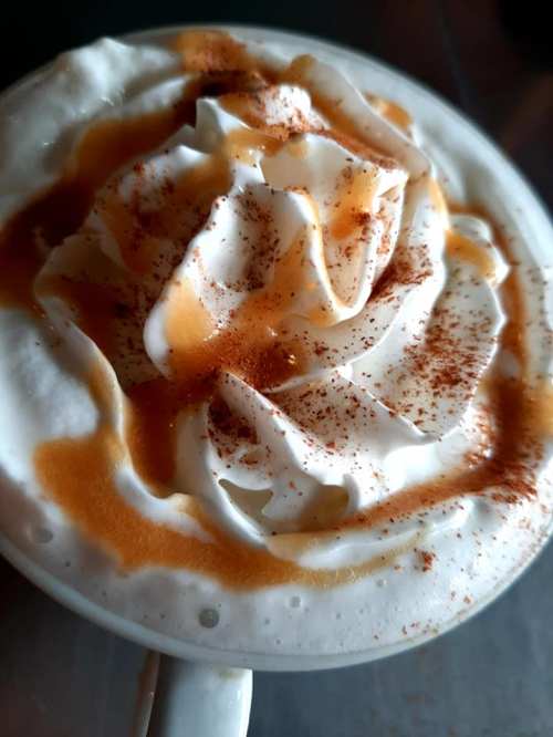 A close-up of a creamy coffee topped with whipped cream, caramel drizzle, and a sprinkle of cinnamon.