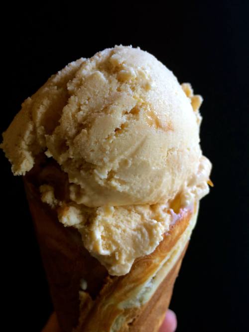 A close-up of a creamy scoop of ice cream in a cone against a dark background.