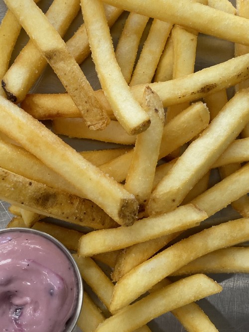 A close-up of golden French fries arranged on a surface, with a small cup of pink dipping sauce beside them.