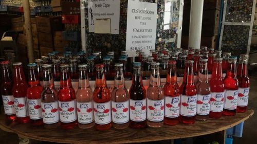 A display of colorful custom soda bottles arranged on a table, promoting Valentine's Day options.