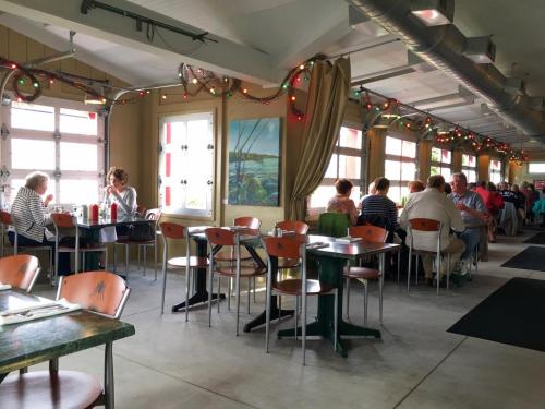 A cozy restaurant interior with patrons seated at tables, large windows, and festive decorations.