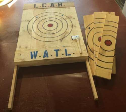 A wooden target board with painted circles and letters, alongside three wooden planks and a small hammer.