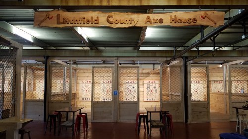 Interior of Litchfield County Axe House with axe-throwing lanes and wooden decor. Tables are set up for spectators.