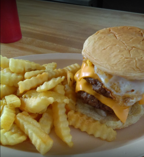 A plate with crinkle-cut fries and a cheeseburger topped with an egg on a bun.