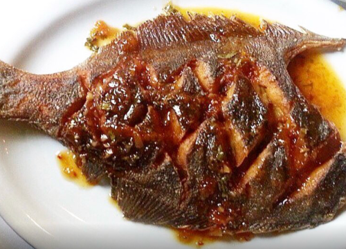 A cooked fish with a glossy sauce, presented on a white plate.