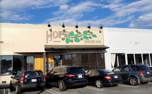 Exterior of Hops Burger Bar with a sign and parked cars in front under a blue sky with clouds.