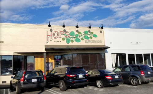 Exterior of Hops Burger Bar with a sign and parked cars in front under a blue sky with clouds.