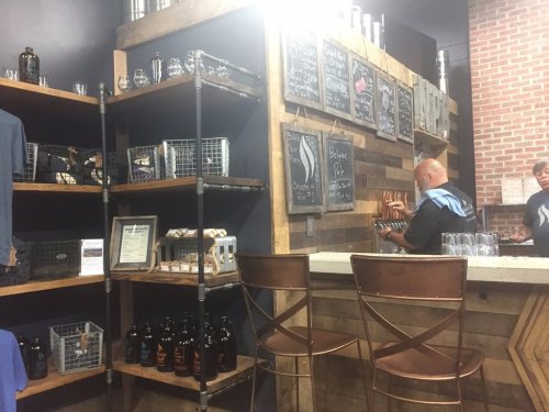 A rustic bar area with wooden shelves, chalkboard menus, and a bartender serving drinks in a cozy setting.