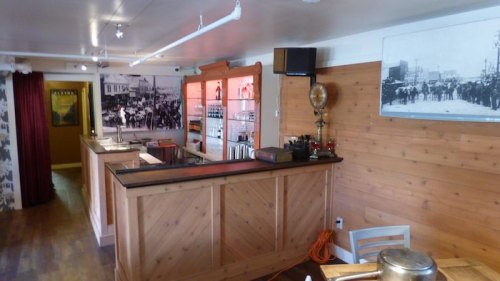 Interior of a rustic bar with wooden decor, shelves of bottles, and historical photos on the walls.