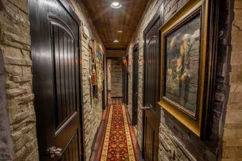 A narrow hallway with stone walls, wooden doors, and framed artwork, featuring a patterned red carpet.