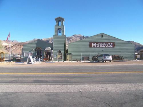 A green building with a clock tower, labeled "Museum," set against a clear blue sky and mountains in the background.