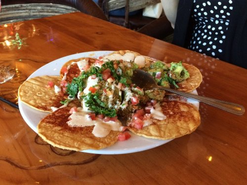 A plate of tacos topped with lettuce, tomatoes, and sauce, served on a wooden table.