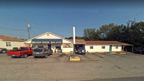 Exterior view of Hilltop Pizza, featuring parked cars and a clear sky.