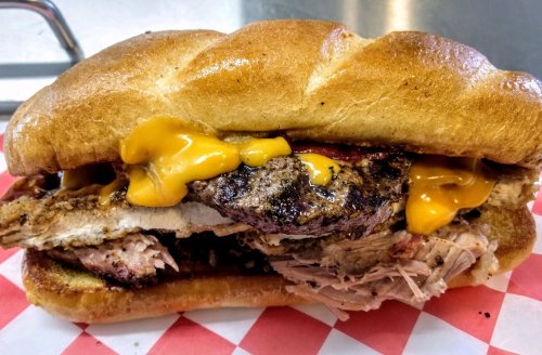 A hearty sandwich with grilled meat, melted cheese, and toppings on a soft bun, served on a checkered paper.