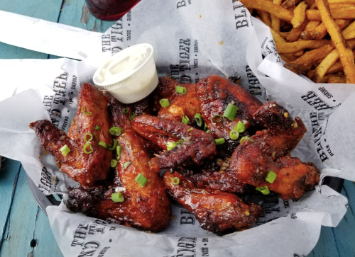 A basket of crispy chicken wings topped with green onions and a side of ranch dressing, served with fries.