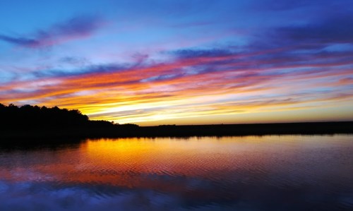 A vibrant sunset over a calm lake, with colorful clouds reflecting on the water's surface.