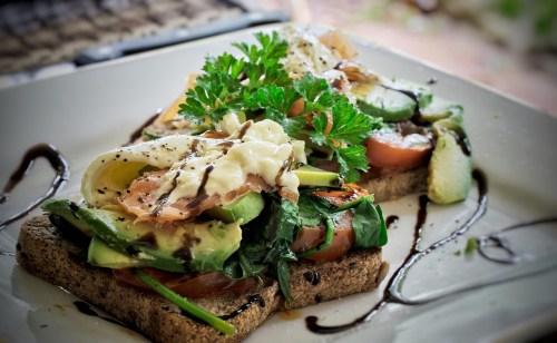 Two slices of whole grain toast topped with spinach, tomatoes, avocado, poached eggs, and drizzled with balsamic glaze.