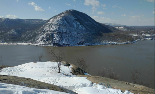 Snow-covered landscape with a mountain and river under a clear blue sky.