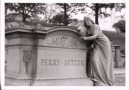 A stone mausoleum with the name "PERRY-SETZER" and a statue of a woman leaning on it, surrounded by trees.