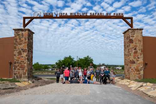 Group of people posing at the entrance of Buena Vista Wildlife Safari RV Park under a cloudy sky.