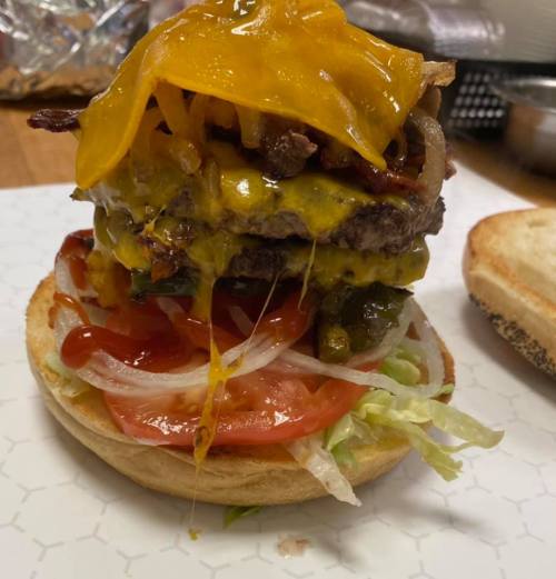 A towering burger with two patties, melted cheese, fried onions, lettuce, tomato, and ketchup on a toasted bun.