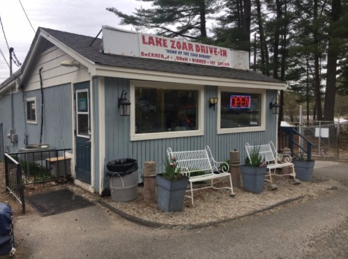 A small blue drive-in restaurant with a sign reading "Lake Zoar Drive-In" and an "OPEN" sign, surrounded by greenery.